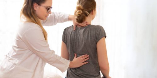 Female physiotherapist or a chiropractor examining patients back. Physiotherapy, rehabilitation concept.